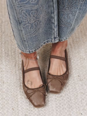 Brown ballet flats worn with blue jeans on a textured surface