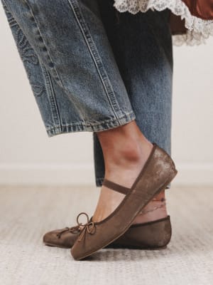 Brown flat shoes worn with rolled-up jeans on a light background