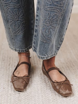 Brown ballet flats worn with blue jeans on a neutral background
