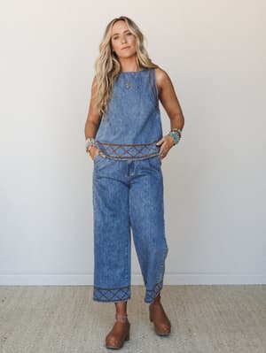 A denim two-piece set in medium wash blue with rich brown cross-stitch embroidery trim, styled with chunky clogs and stacked turquoise and silver bracelets — the kind of put-together outfit that looks effortless but absolutely isn't by accident.