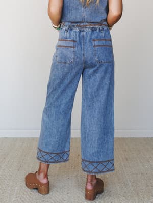 Back view of wide-leg cropped denim pants with rich brown embroidered trim at the hem and waistband, paired with a matching denim top and brown platform clogs — the kind of set that does all the work for you.
