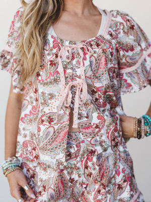 A close-up torso shot of a paisley-printed matching set with lace-up tie detail at the center front, styled with stacked beaded and turquoise bracelets — soft, boho, and very much the kind of outfit you'd pack first.