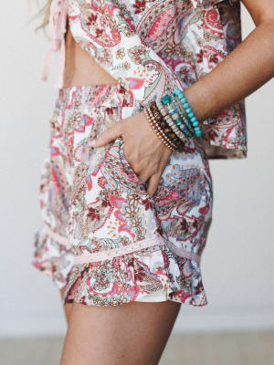 A close-up of a paisley-print matching set — cropped top and ruffled shorts — styled with a stack of beaded bracelets, giving off easy summer energy with a boho soul.