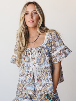 A breezy paisley set in powder blue shot against a clean studio backdrop — the flutter sleeves and lace tie front give it that effortless, just-threw-it-on feeling that somehow looks completely intentional.