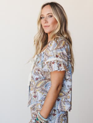 A soft side-profile shot of a model in a matching paisley printed set — powder blue with warm rust and gold tones — styled with stacked turquoise bracelets and a delicate lace-trim detail that gives the whole look a quietly romantic, boho-at-brunch e