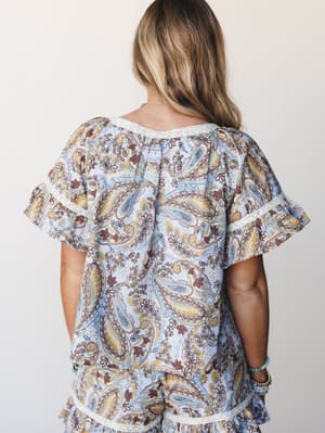 A back-view shot of a matching paisley set in powder blue — the flutter-sleeve top has lace trim detailing at the neckline and sleeves, paired with coordinating shorts that echo the same lace hem, giving the whole look a relaxed, vintage-boho feel.