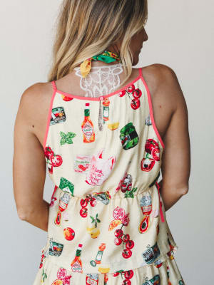A back-view shot of a butter yellow short set covered in a playful illustrated food print — Tabasco bottles, tomatoes, cherries, and pantry staples — with coral piping trim, lace detail at the upper back, and a relaxed elastic waist that makes it fee