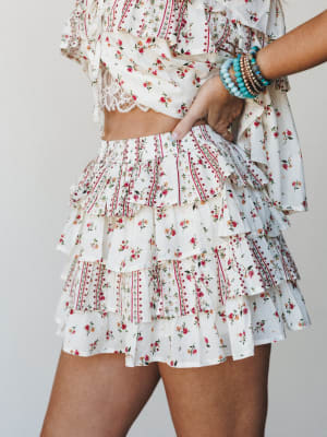 A flirty tiered ruffle skort in a cream ditsy floral print styled with a matching crop top and stacked turquoise bracelets — the kind of outfit that makes a Tuesday feel like a road trip.