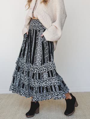 A tiered black and white floral maxi skirt styled with an oversized cream knit sweater and black block-heel ankle boots — the kind of outfit that looks like it came together effortlessly but definitely did not.
