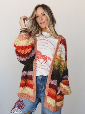 A chunky, multicolor striped knit cardigan styled over a vintage-inspired graphic tee and embroidered jeans — the kind of outfit that looks like it came together effortlessly but you know she thought about it.