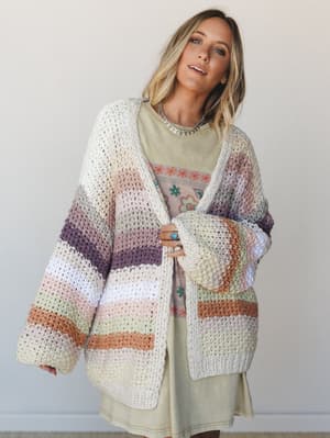 An oversized chunky knit cardigan in multicolor stripes layered over a sage green graphic tee dress — the kind of outfit that looks like it came together effortlessly but you know she thought about it.