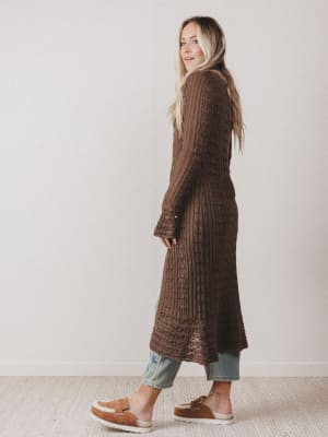 Woman wearing a long brown knitted cardigan against a plain background