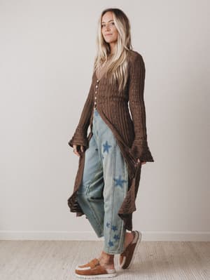 Woman wearing a brown ribbed sweater and blue jeans with star patterns indoors.