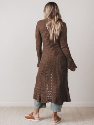 Woman wearing a long brown knitted cardigan against a plain background