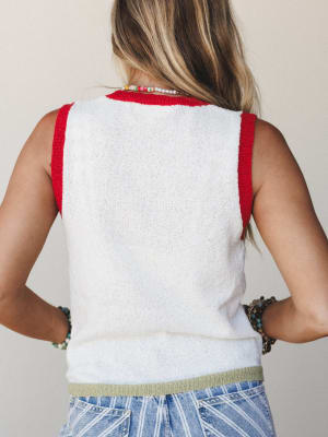 Back view of a cropped knit tank in off-white with red contrast trim at the neckline and armholes and a sage green ribbed hem, styled with printed wide-leg jeans and layered beaded jewelry.