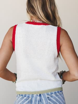 Back view of a cropped knit tank in off-white with red contrast trim at the neckline and armholes and a sage green ribbed hem, styled with printed wide-leg jeans and layered beaded jewelry.