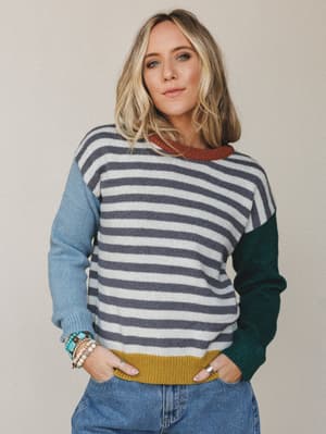 A color-block striped knit sweater styled with denim and layered bracelets — the kind of sweater that looks like it was borrowed from somewhere cool and never given back.