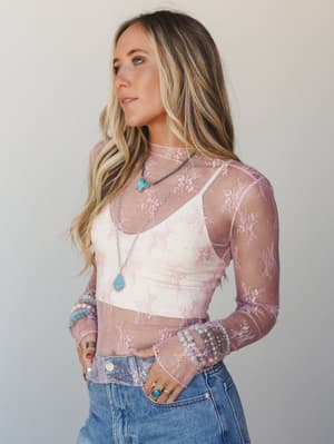 A sheer blush lace long-sleeve top layered over a white bralette, styled with denim and stacked turquoise jewelry — effortlessly romantic with a laid-back boho edge.