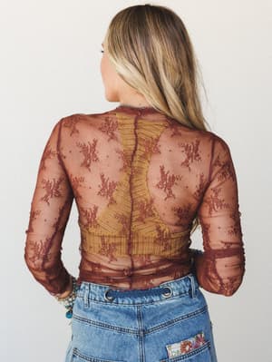 Shot from behind, this sheer lace layering top in deep red bean shows off its floral embroidery and semi-transparent construction over a mustard bralette, styled with patched denim jeans — effortlessly expressive and a little romantic.