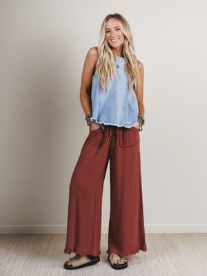 Woman wearing a light blue sleeveless top and red patterned pants against a plain background
