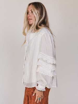 Woman wearing a white blouse with lace details on a plain background
