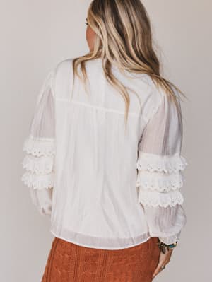 Woman wearing a white blouse with lace details on a plain background