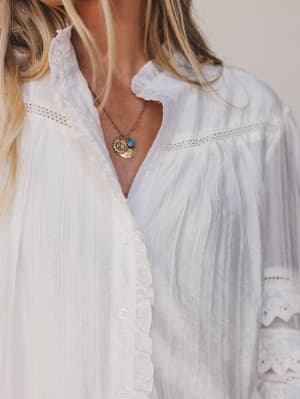 Person wearing a white blouse with a necklace featuring a circular pendant.