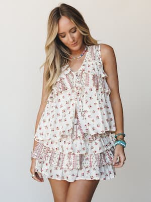 A flowy floral two-piece set in cream and rose — tiered ruffles, a tie-front top, and a mini skirt that moves like it was made for a long summer afternoon.