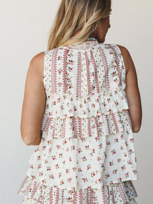 A back-view close-up of a sleeveless floral top in ivory with tiered ruffle detailing and a lace back yoke — the kind of top that looks effortless and intentional at the same time.