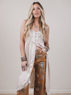 Woman wearing a white sleeveless top and brown floral pants against a plain background