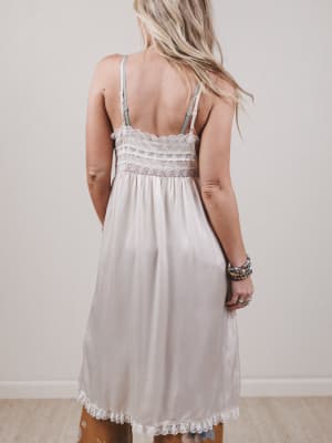 Woman wearing a light-colored dress with lace details against a plain background