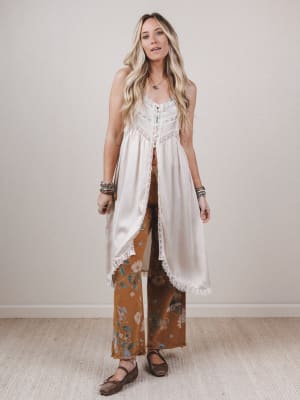 Woman wearing a white top and brown floral pants against a plain background