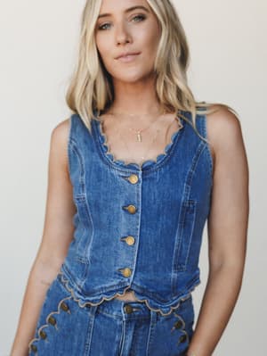 A denim vest top with scalloped edges and gold button-front closure styled as a coordinating set — effortlessly Western-meets-boho with delicate layered necklaces and an easy, confident expression.