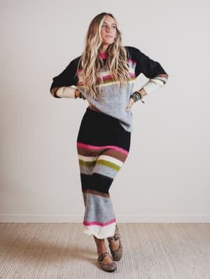 Woman wearing a colorful striped sweater and skirt against a plain background