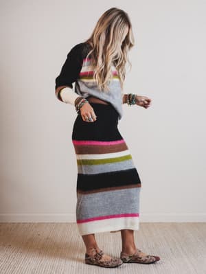 Woman wearing a long, multicolored striped sweater dress against a plain background