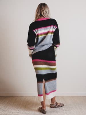 Woman wearing a long, colorful striped sweater and skirt with a plain background