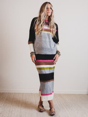 Woman wearing a long, patterned sweater and skirt with a neutral background