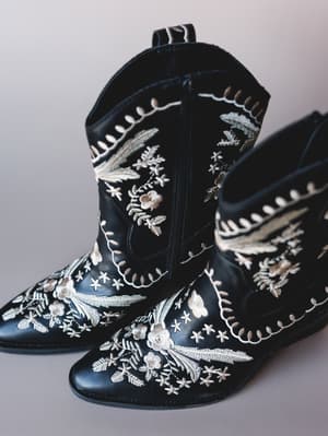 A pair of black western-style ankle booties covered in intricate cream and taupe floral embroidery — the kind of boots that do half the outfit work for you.