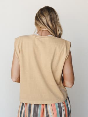 A back-view shot of a sandy, washed-out muscle tank layered over a white top, paired with a multicolor striped skirt — relaxed and easy, the kind of outfit that looks just as good at a farmers market as it does on a beach boardwalk.