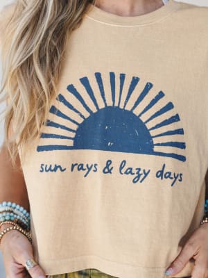 A sun-washed muscle tank in faded mustard with a distressed navy sunrise graphic and 'sun rays & lazy days' script — styled with stacked turquoise and beaded bracelets for that effortless, been-outside-all-day energy.