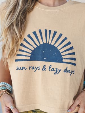 A sun-washed muscle tank in faded mustard with a distressed navy sunrise graphic and 'sun rays & lazy days' script — styled with stacked turquoise and beaded bracelets for that effortless, been-outside-all-day energy.