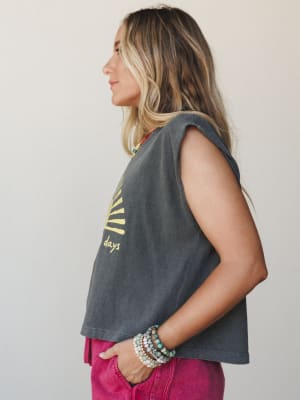 A sun-washed charcoal muscle tank with a yellow sun rays graphic gets styled with fuchsia jeans and a stack of beaded bracelets — the kind of effortless summer outfit that looks like it came together in five minutes but somehow just works.
