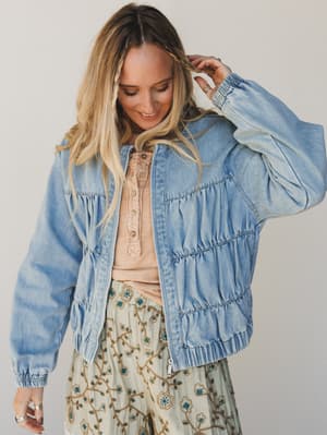 Woman wearing a light blue denim jacket over a patterned dress against a plain background