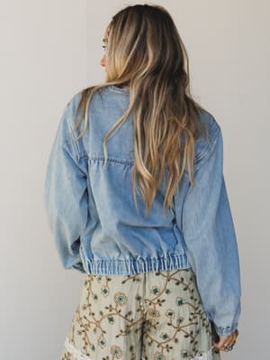 Person wearing a denim jacket with a plain background