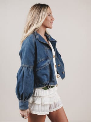 Woman wearing a denim jacket and white skirt against a plain background