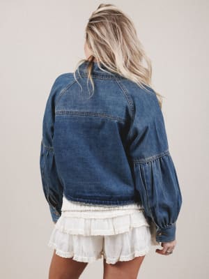 Person wearing a blue denim jacket and white lace dress on a beige background