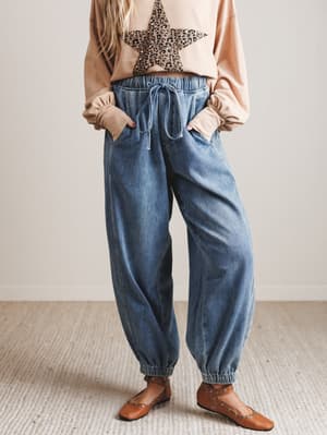 Person wearing a leopard print top, beige cardigan, blue jeans, and brown shoes on a neutral background