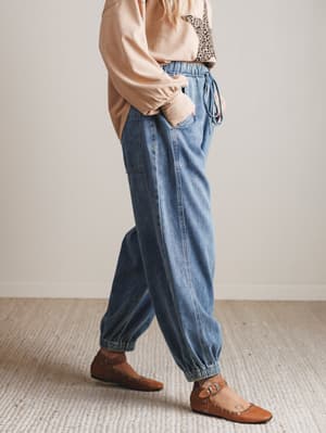 Person wearing blue jeans and a beige top in a minimal indoor setting