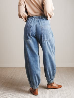Person wearing blue jeans and a beige top in a minimal indoor setting