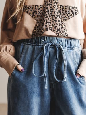 Person wearing a leopard print top and blue jeans with a neutral background